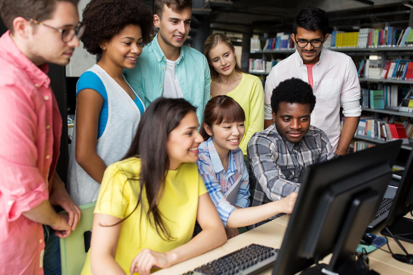 A diverse group of students gathered around a computer, learning together